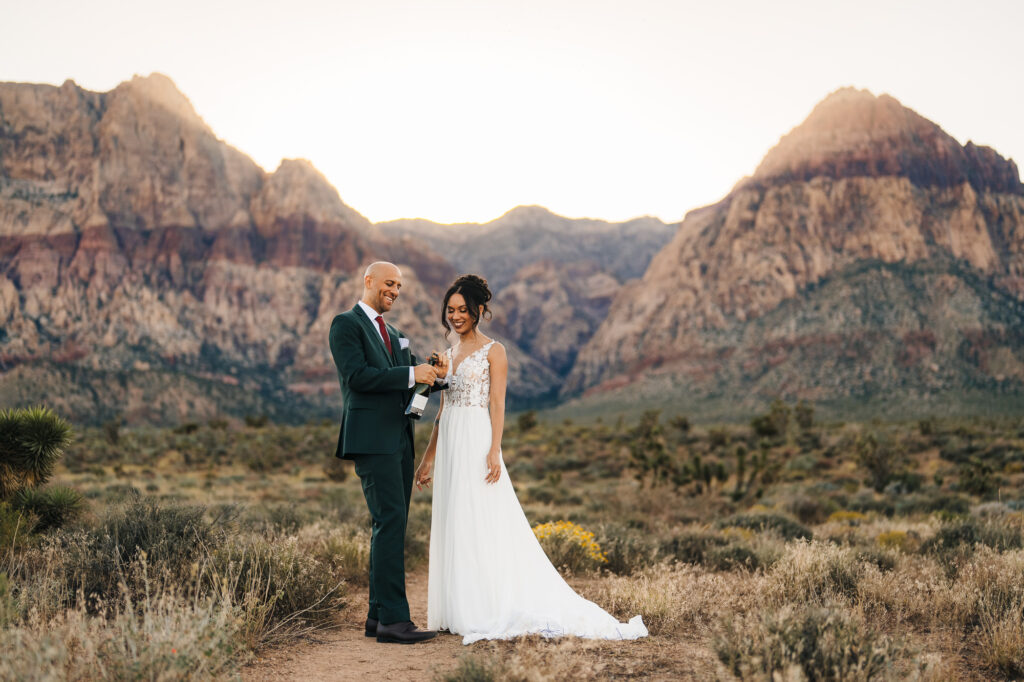 A delightful eloping couple popping open a bottle of champagne amidst the stunning beauty of Red Rock Canyon in Las Vegas.