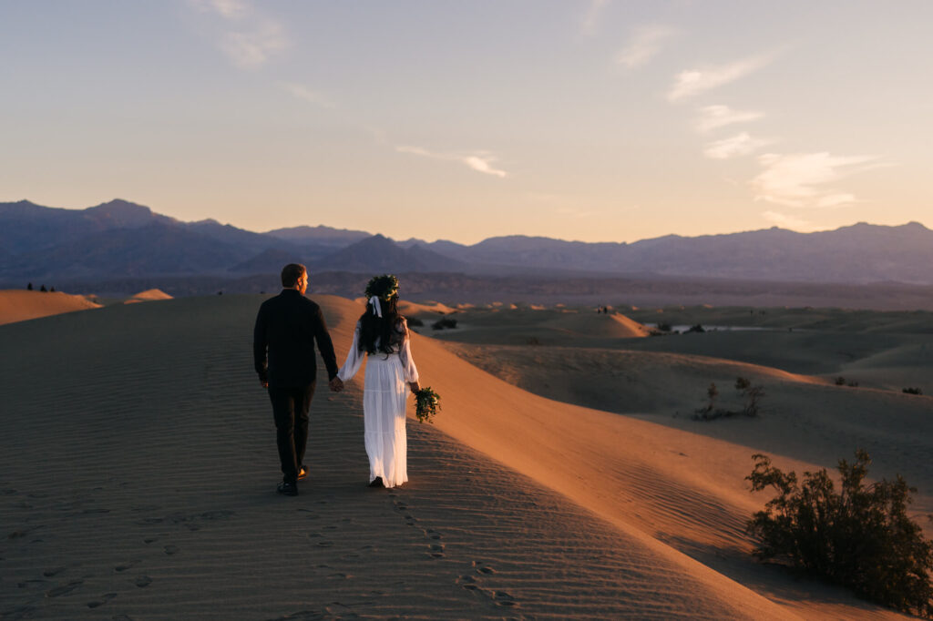 A delightful couple strolling hand in hand amid the sunrise, celebrating their elopement at Mesquite Sand Dunes in Death Valley National Park.