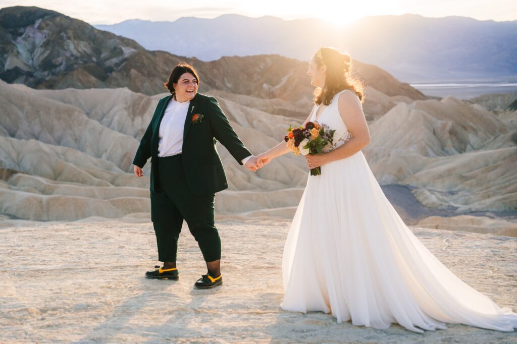 A blissful couple strolling hand in hand, happily gazing at each other during their elopement sunset at Zabriskie Point in Death Valley National Park.