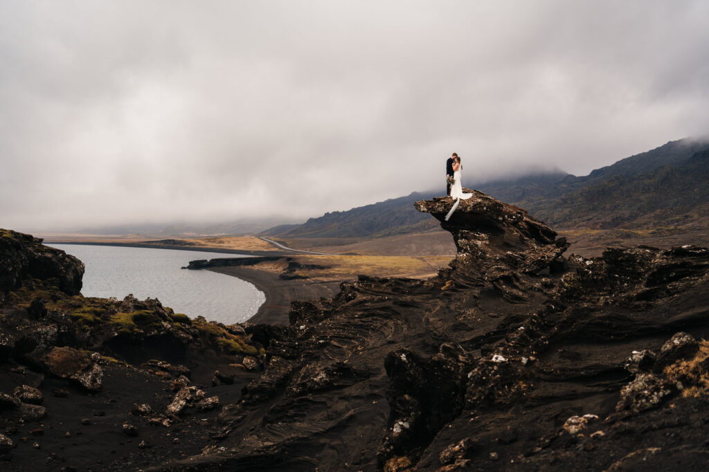 Couple standing against a breathtaking backdrop of majestic mountains and a serene ocean, capturing the essence of their epic elopement in Iceland. How to elope in Iceland.