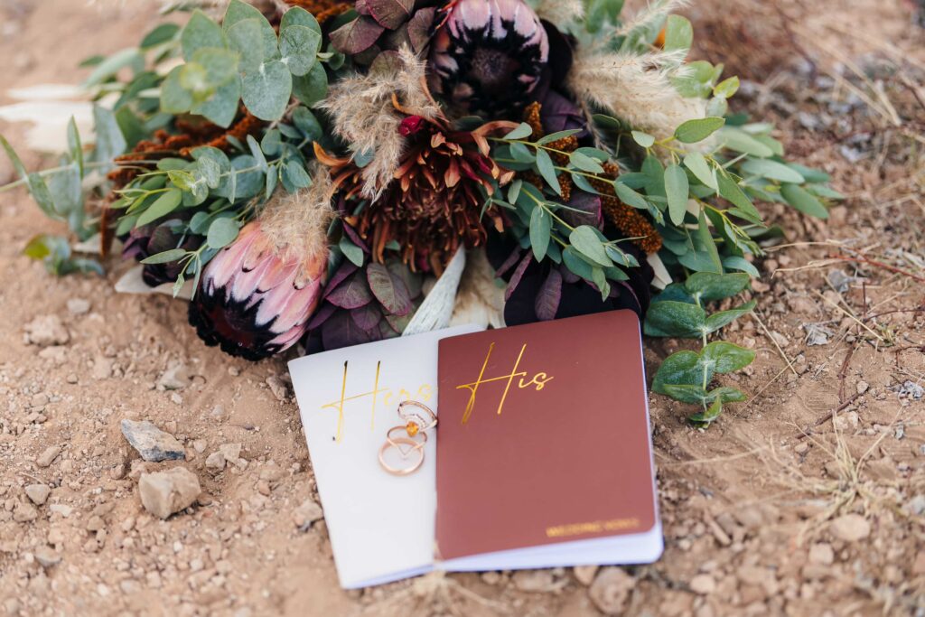 A beautiful flower arrangement complemented by a wedding vows notebook and wedding rings.