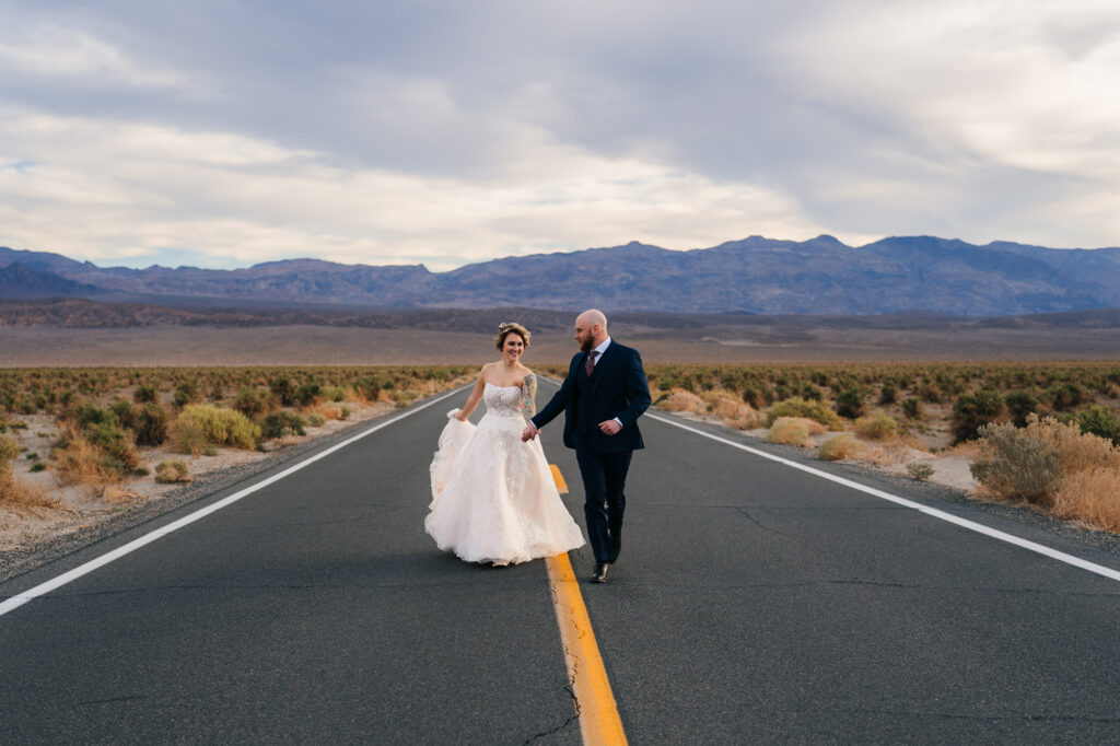 A playful couple joyfully running on the road at Devil's Cornfield in Death Valley National Park, embracing the adventure of their elopement.