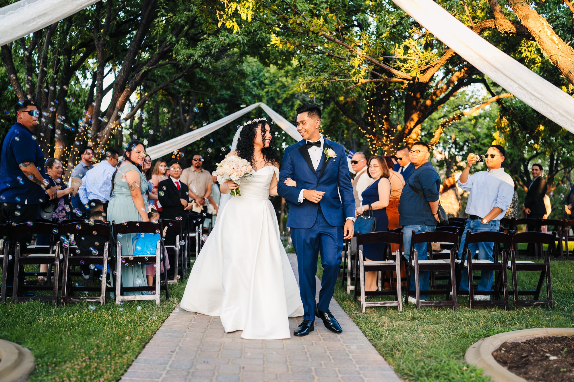 Couple walking down the aisle and looking at each other smiling after their outdoor wedding ceremony at The Grove in Las Vegas.