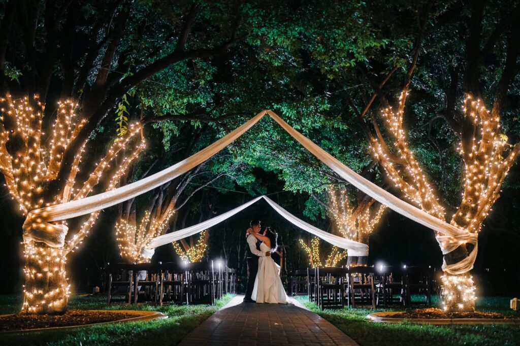 Stunning photo of a newlywed couple sharing an intimate moment under a tree with the string lights on at night after their wedding at The Grove in Las Vegas.